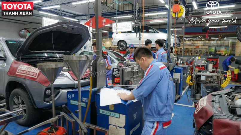 Đội ngũ kỹ thuật viên của Toyota Thanh Xuân, với đồng phục chuyên nghiệp và thái độ tận tâm, đang kiểm tra xe trong một khoang dịch vụ hiện đại.